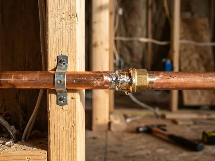 A close daylight detail of a bright soldered copper joint on a new water line, the pipe strapped to a stud, no people
